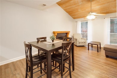 Dining area featuring vaulted ceiling, wood ceiling, light wood-style flooring, a ceiling fan, and a fireplace