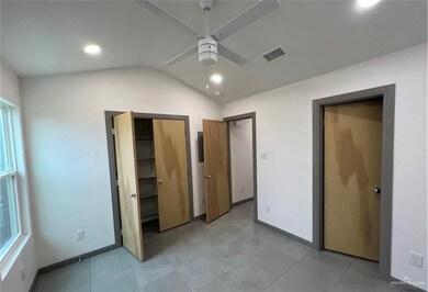 Unfurnished bedroom featuring light tile patterned flooring, vaulted ceiling, visible vents, baseboards, and a ceiling fan