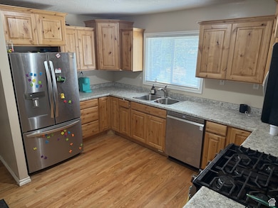 Kitchen featuring appliances with stainless steel finishes, a sink, light wood-type flooring, light countertops, and light brown cabinets