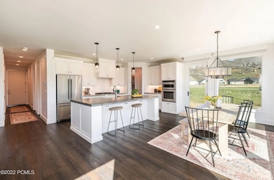 Kitchen featuring white cabinets, a kitchen bar, appliances with stainless steel finishes, a center island with sink, and hanging light fixtures