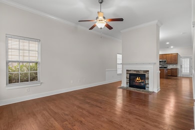Unfurnished living room with dark wood-style floors, ornamental molding, a fireplace with flush hearth, and a ceiling fan