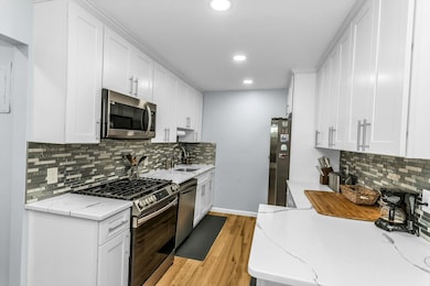 Kitchen with appliances with stainless steel finishes, white cabinets, light wood-type flooring, backsplash, and recessed lighting