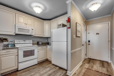 Kitchen with dark stone countertops, ornamental molding, white appliances, and light hardwood / wood-style floors
