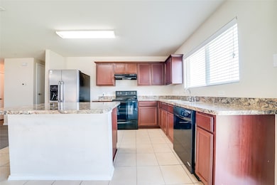 Kitchen with black appliances, a center island, light tile patterned floors, and light countertops