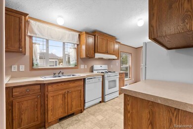 Kitchen with brown cabinetry, white appliances, light countertops, crown molding, and a textured ceiling