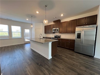 Kitchen with appliances with stainless steel finishes, tasteful backsplash, dark brown cabinets, a center island with sink, and decorative light fixtures