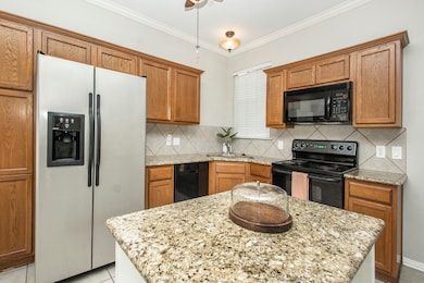 Kitchen featuring brown cabinets, black appliances, tasteful backsplash, crown molding, and light tile patterned floors