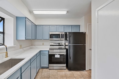 Kitchen with stainless steel appliances, light stone counters, light tile patterned floors, and blue cabinets
