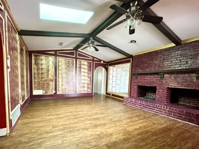 Unfurnished living room featuring wood finished floors, a skylight, a fireplace, and arched walkways