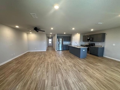 Kitchen featuring appliances with stainless steel finishes, open floor plan, a center island with sink, wood finished floors, and ceiling fan