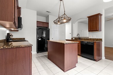 Kitchen featuring black appliances, a center island, light tile patterned floors, and dark stone counters
