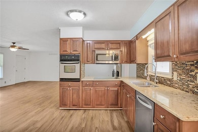 Kitchen with stainless steel appliances, a sink, light wood-style flooring, brown cabinetry, and a textured ceiling