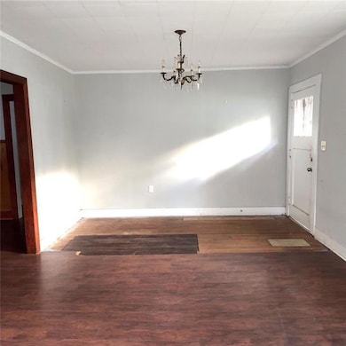 Unfurnished dining area with dark wood-style floors, crown molding, and a chandelier