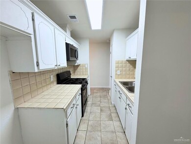 Kitchen with tile countertops, black gas range oven, decorative backsplash, white cabinets, and stainless steel microwave