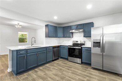 Kitchen with a sink, appliances with stainless steel finishes, a peninsula, under cabinet range hood, and blue cabinetry
