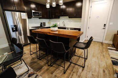 Kitchen with butcher block counters, stainless steel appliances, light wood finished floors, hanging light fixtures, and dark brown cabinets