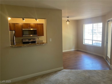 Kitchen with stainless steel appliances, carpet, brown cabinets, dark stone countertops, and decorative light fixtures