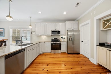 Kitchen with stainless steel appliances, ornamental molding, hanging light fixtures, light stone countertops, and light wood-type flooring