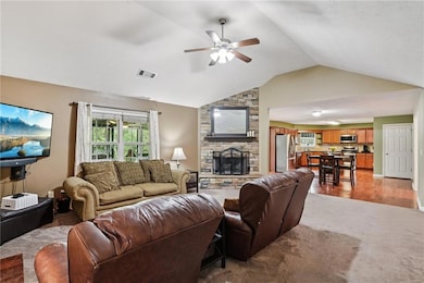 Living area featuring a ceiling fan, vaulted ceiling, a fireplace, and light colored carpet