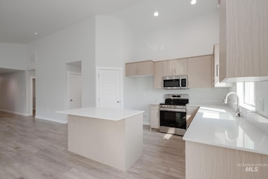 Kitchen with high vaulted ceiling, light brown cabinets, appliances with stainless steel finishes, a center island, and light wood-type flooring