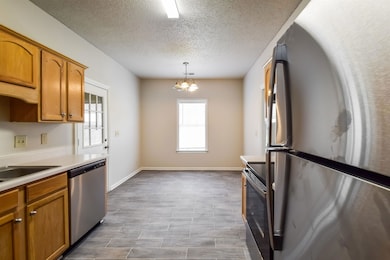Kitchen featuring stainless steel appliances, brown cabinetry, light countertops, pendant lighting, and a textured ceiling