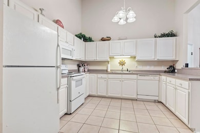 Kitchen with white appliances, light tile patterned flooring, white cabinets, decorative light fixtures, and a high ceiling