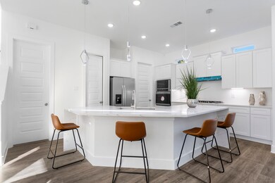 Modern kitchen featuring a spacious island, quartz countertops, built-in appliances, and stylish pendant lighting.