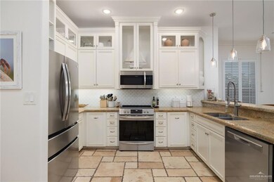 Kitchen featuring stainless steel appliances, decorative light fixtures, light stone counters, white cabinetry, and ornamental molding