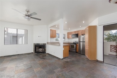 Kitchen featuring open floor plan, stainless steel appliances, ceiling fan, light countertops, and stone tile flooring