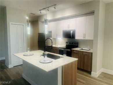 Kitchen with white cabinets, stainless steel appliances, light wood-style floors, an island with sink, and rail lighting