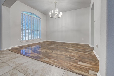 Empty room featuring arched walkways, wood finished floors, a chandelier, and a textured wall