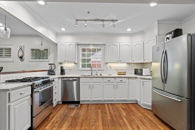 Kitchen with appliances with stainless steel finishes, white cabinetry, ornamental molding, dark wood-type flooring, and light stone counters