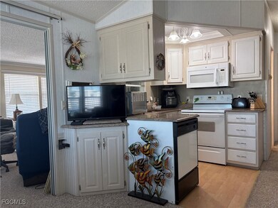 Kitchen featuring white appliances, dark stone countertops, a textured ceiling, vaulted ceiling, and white cabinets