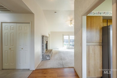 Hallway featuring light colored carpet, light wood-style floors, a textured ceiling, and vaulted ceiling