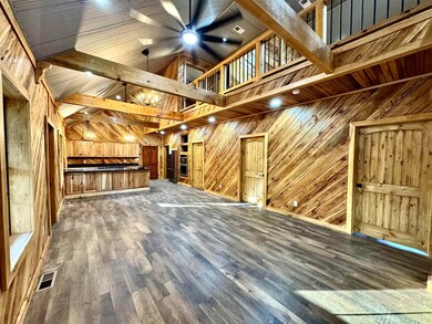 Unfurnished living room featuring wooden walls, ceiling fan, wood finished floors, a chandelier, and beamed ceiling