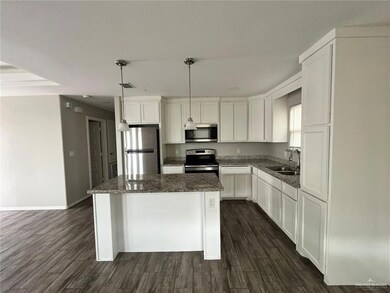Kitchen featuring a kitchen island, appliances with stainless steel finishes, white cabinetry, dark wood finished floors, and dark stone countertops