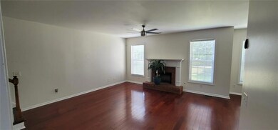 Unfurnished living room featuring healthy amount of natural light, a ceiling fan, wood-type flooring, and a brick fireplace