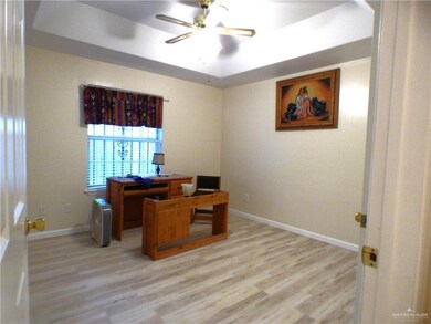 Home office with baseboards, light wood-style flooring, ceiling fan, and a tray ceiling
