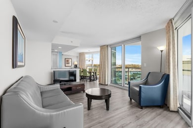 Living room with a wall of windows, a notable chandelier, a textured ceiling, and light wood-type flooring