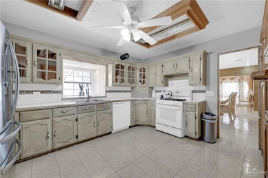 Kitchen with white appliances, light countertops, a sink, ceiling fan, and glass insert cabinets