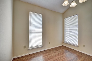 Unfurnished room featuring a textured ceiling, wood finished floors, lofted ceiling, a textured wall, and plenty of natural light