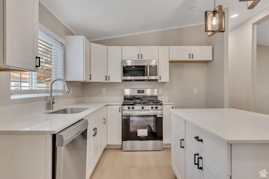 Kitchen featuring appliances with stainless steel finishes, ornamental molding, white cabinetry, light stone counters, and a center island
