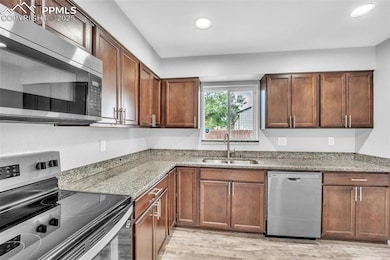 Kitchen with appliances with stainless steel finishes, recessed lighting, light wood finished floors, and light stone counters