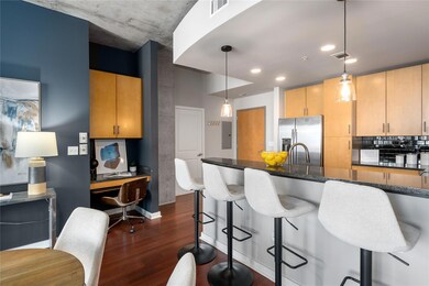 Kitchen featuring stainless steel fridge, dark wood-style flooring, dark stone countertops, a kitchen bar, and decorative light fixtures