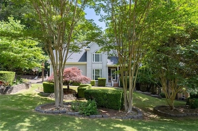 View of property hidden behind natural elements with a front yard, stucco siding, and a shingled roof