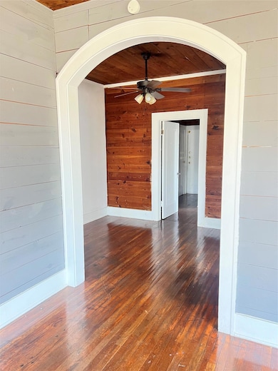Unfurnished room featuring arched walkways, wooden walls, hardwood / wood-style flooring, a ceiling fan, and wooden ceiling