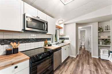 Kitchen with wood counters, appliances with stainless steel finishes, lofted ceiling, white cabinetry, and decorative backsplash