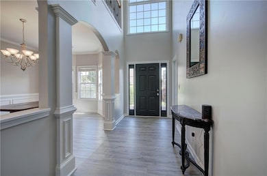 Entryway featuring decorative columns, arched walkways, wood finished floors, a high ceiling, and a chandelier