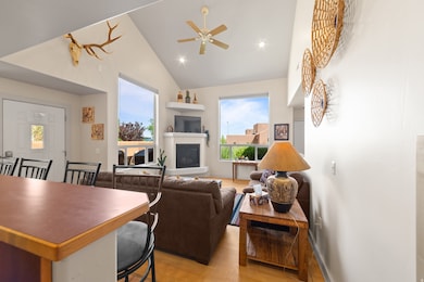 Living area with light wood finished floors, a glass covered fireplace, ceiling fan, and high vaulted ceiling