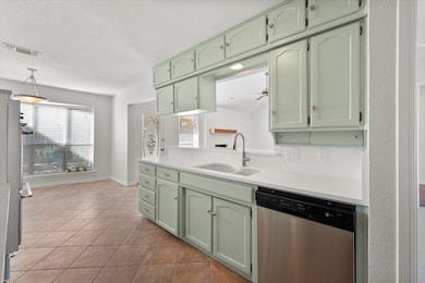 Kitchen with green cabinets, stainless steel dishwasher, plenty of natural light, and light stone counters